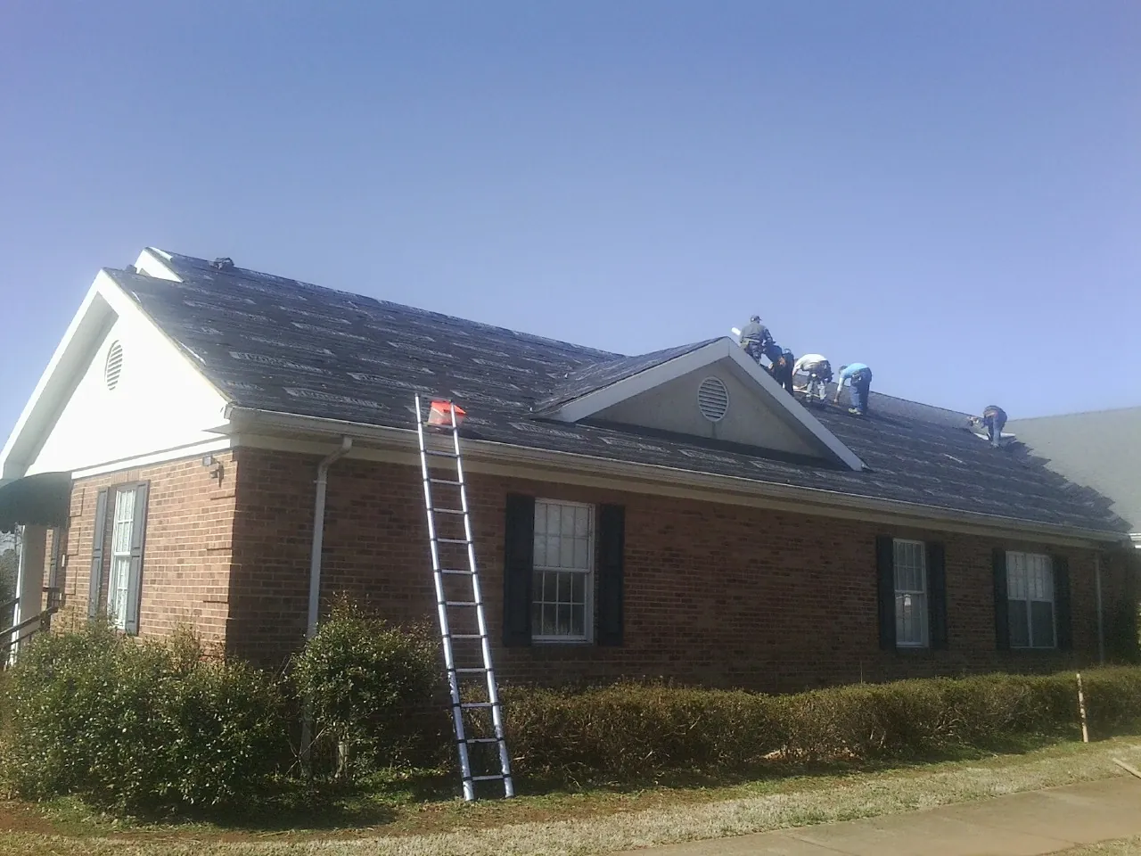 Crew tearing shingles off a brick ranch roof with a ladder set — Emergency Roof Repair work by our crew in Yoder