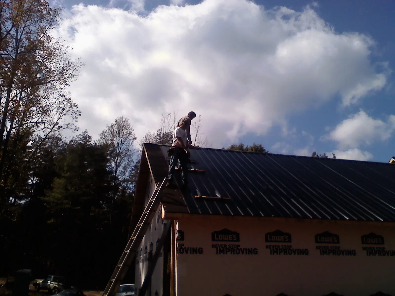 Roofer fastening dark metal panels high against a cloudy sky, from a Roof Inspection job in Yoder
